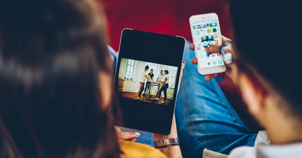 Duas pessoas olham fotos em tablet e celular, o que se relaciona ao memorial virtual.