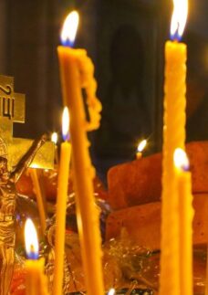 Velas acesas diante de crucifixo dourado, representando o simbolismo do fogo e a fé.