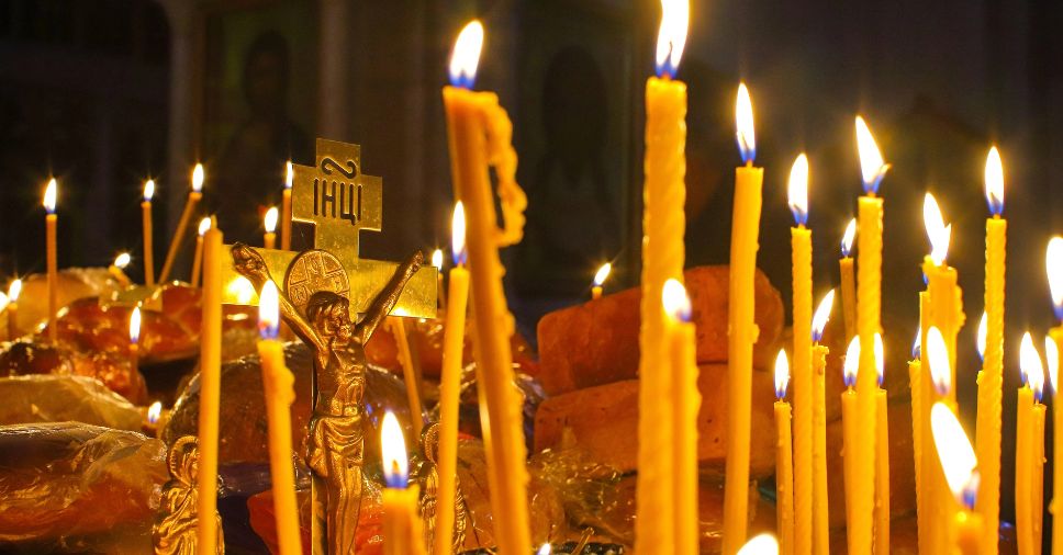 Velas acesas diante de crucifixo dourado, representando o simbolismo do fogo e a fé.