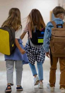 Quatro crianças de costas caminhando com mochilas passando pela morte em fase escolar.
