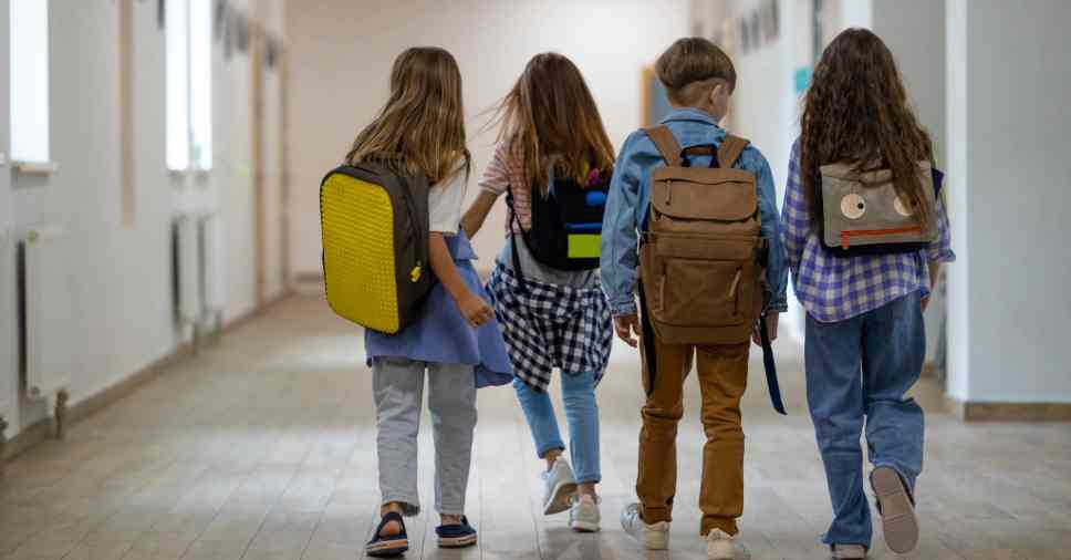 Quatro crianças de costas caminhando com mochilas passando pela morte em fase escolar.